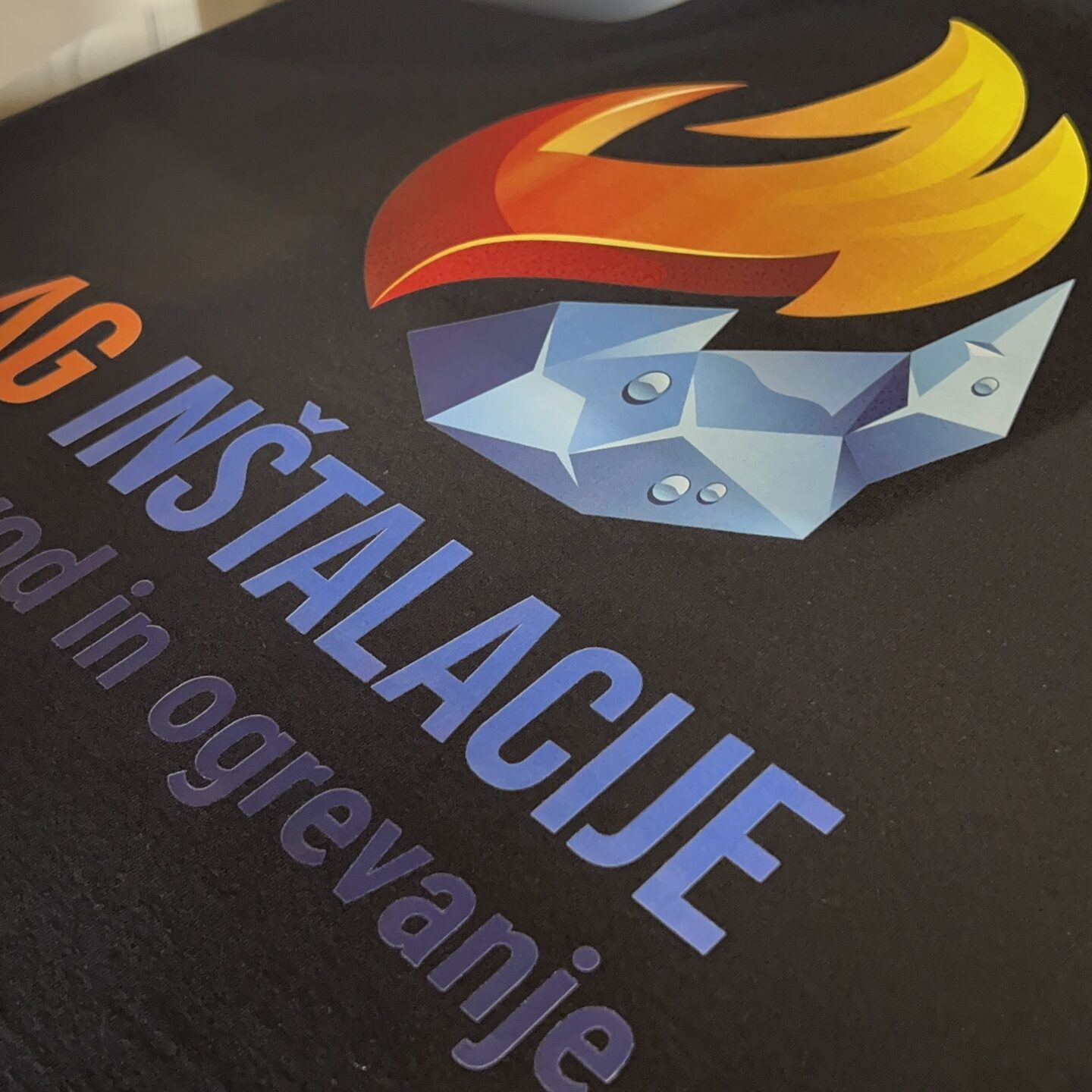 Toplotni transfer logotipa AG Inštalacije na črno majico – kakovosten tisk na tekstil