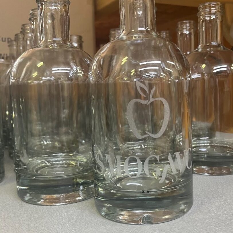 Steklene steklenice s personaliziranim laserskim graviranjem logotipa 'Smogavc' in simbola jabolka