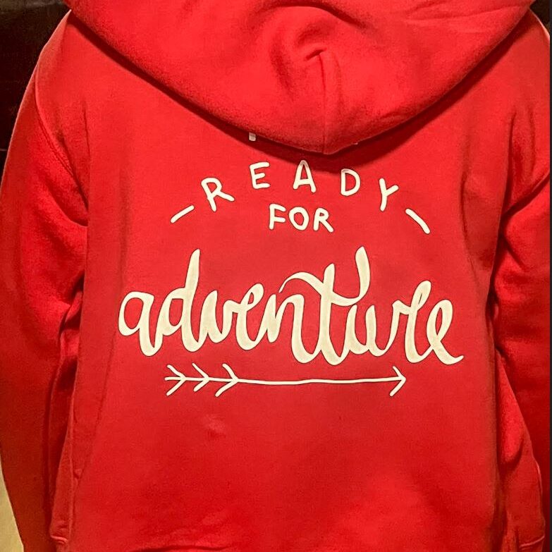 Toplotni transfer z napisom 'Ready for Adventure' na rdečo jopico.